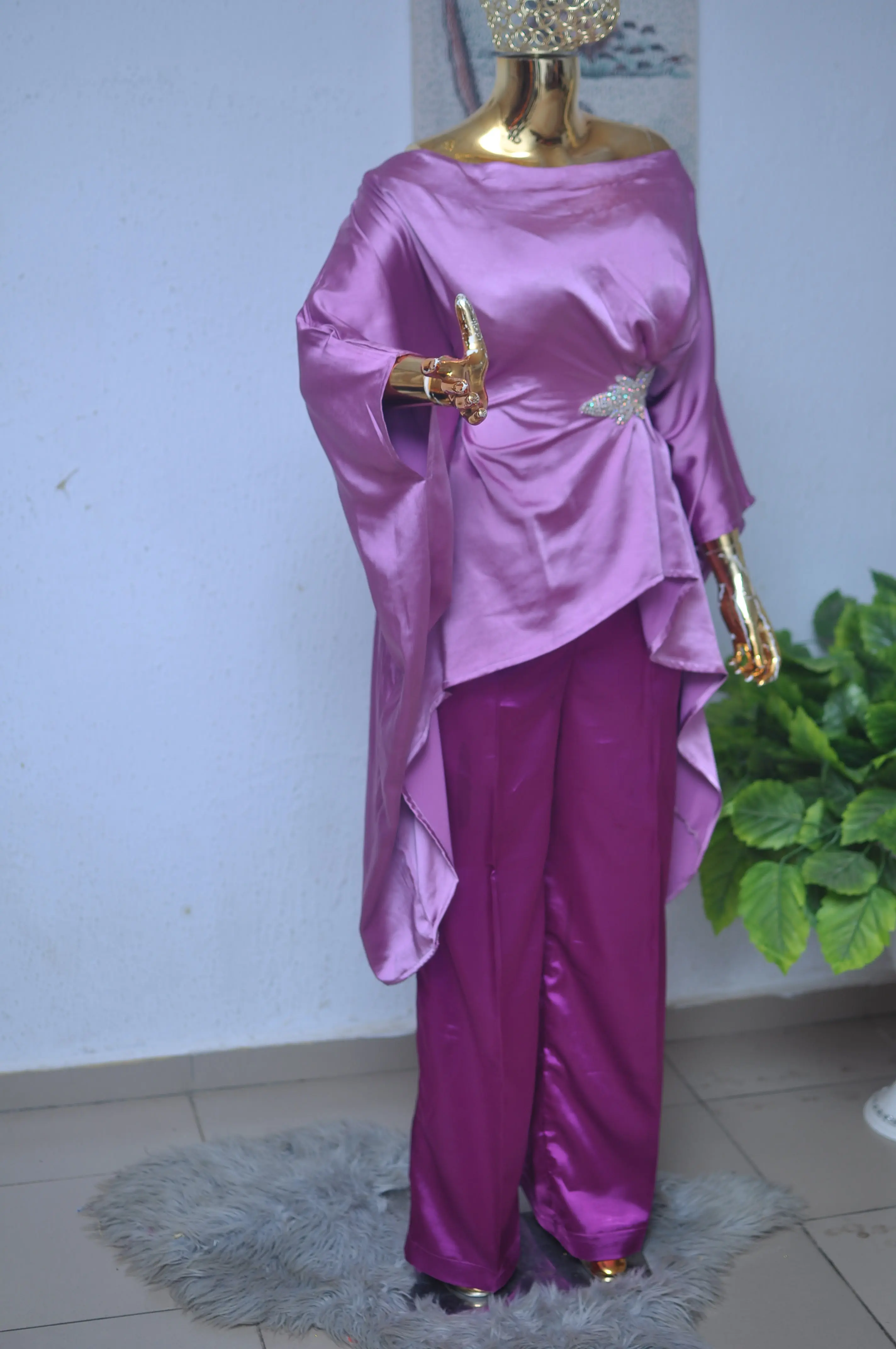 Mauve satin asymmetric top with a crystal brooch, worn with magenta wide-leg trousers.