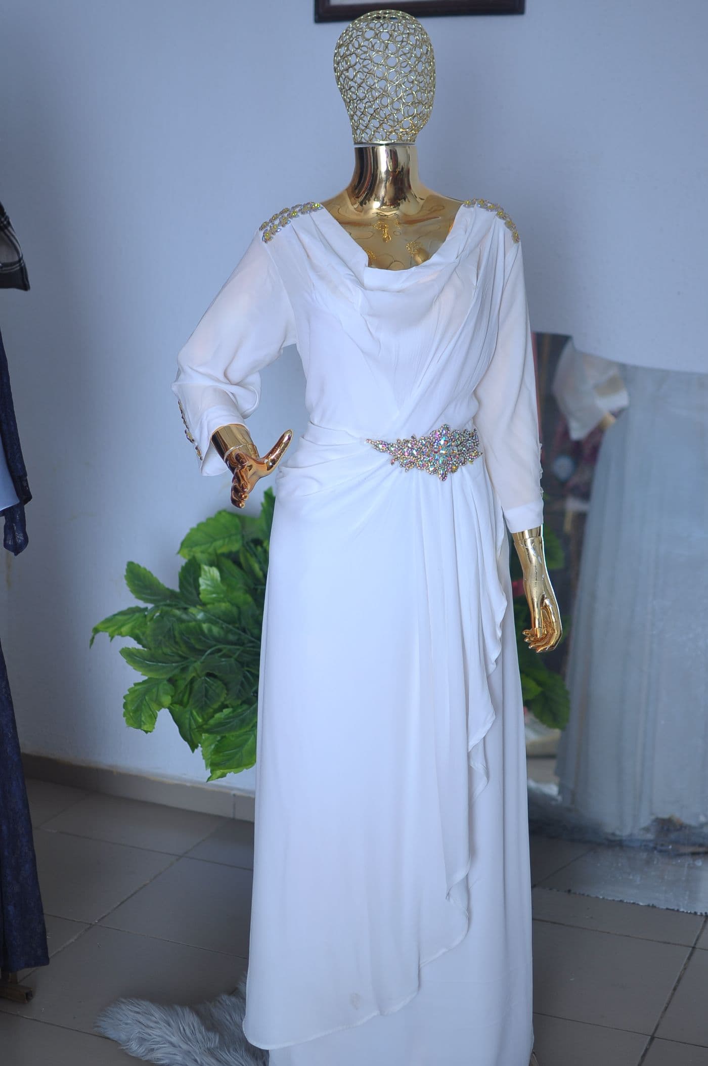 Ivory satin gown with draped cowl neck and crystal waist detail, on a gold mannequin.
