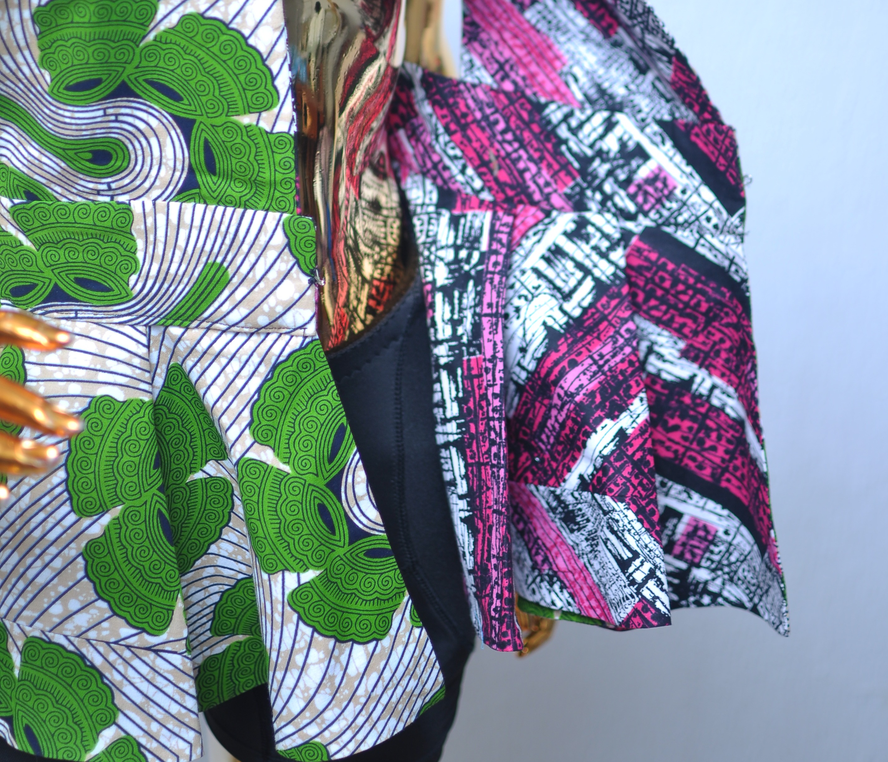 Close-up of a reversible Ankara jacket showing two contrasting prints at once — a green swirl-print exterior against a pink and black geometric lining.